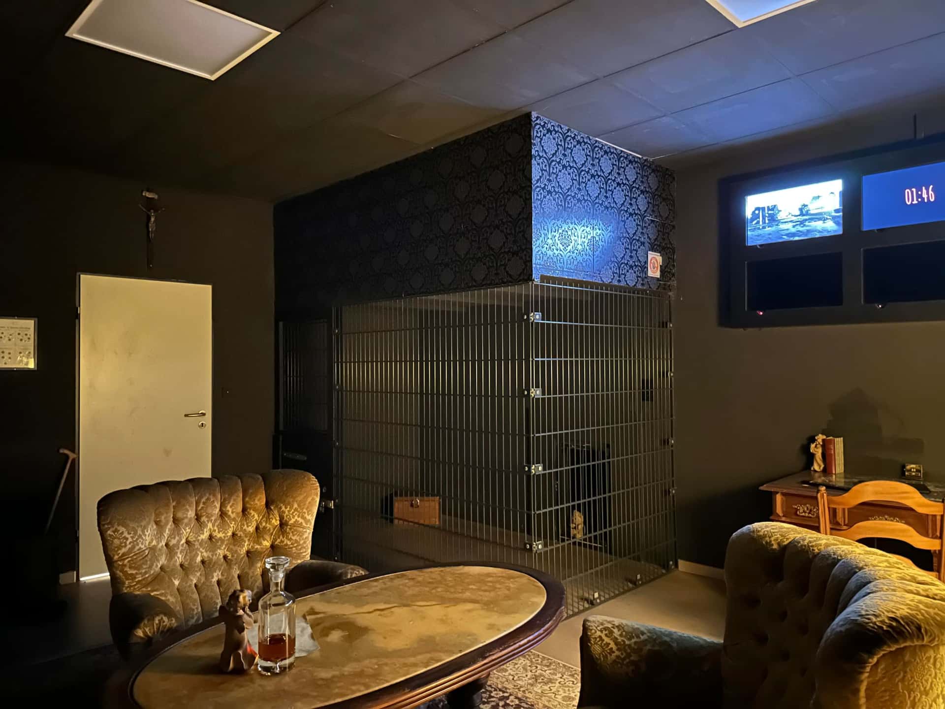 Sessel und vergitterte Zelle im Wohnzimmer im Escape Room Blutrausch in Rosenheim