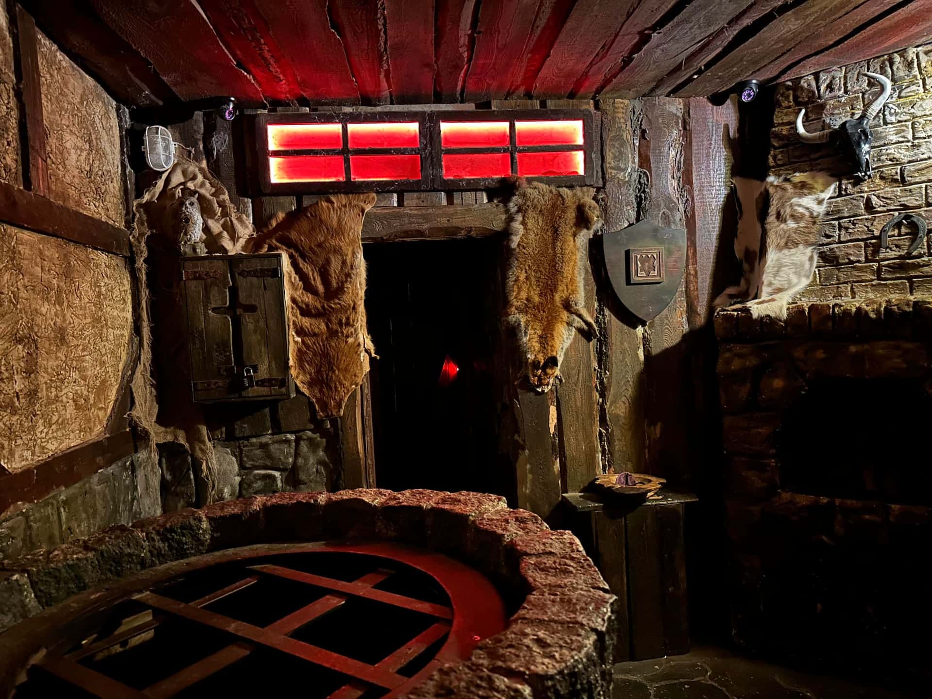 Brunnen mit Gitterabdeckung vor fellbehängter Tür im Escape Room Der Henker in Rosenheim
