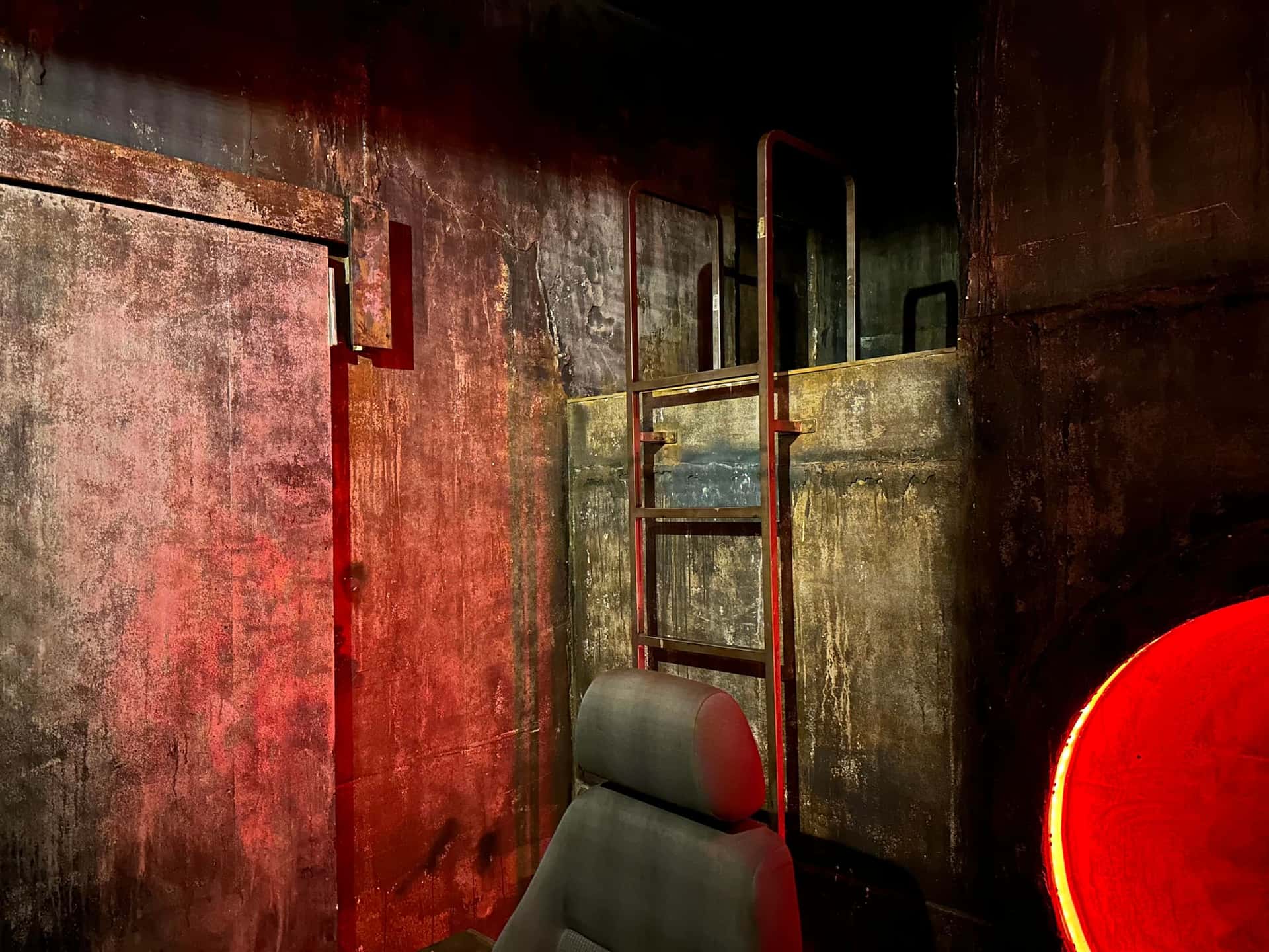 Rostige Wand mit Leiter, Autositz und rotem Lichtring im Escape Room Robot Paranoia in Rosenheim