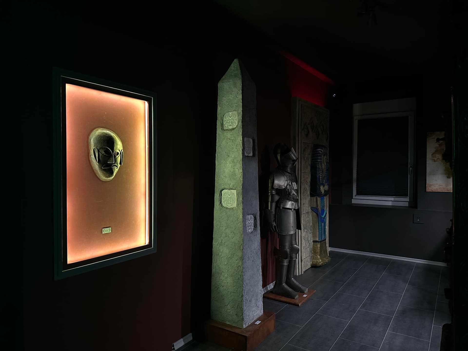 Beleuchtete goldene Maske im Wandrahmen, Obelisk und Ritterrüstung im Lagerraum im Escape Room Artefakt in Rosenheim