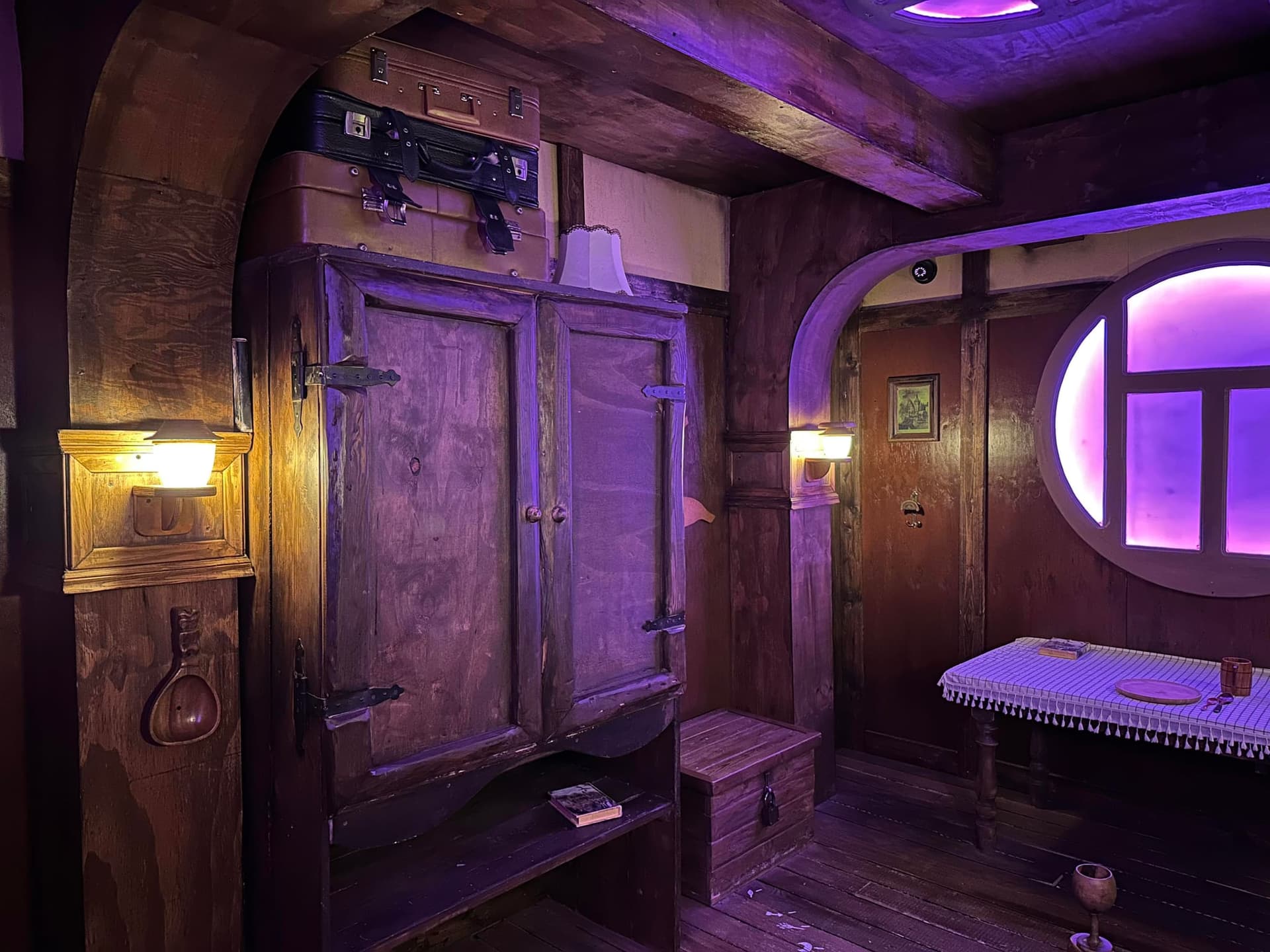 Gemütliche Halblingshütte mit Holzschrank, rundem Fenster und gedecktem Tisch im Escape Room Die Abenteuer des Halbling in Rosenheim