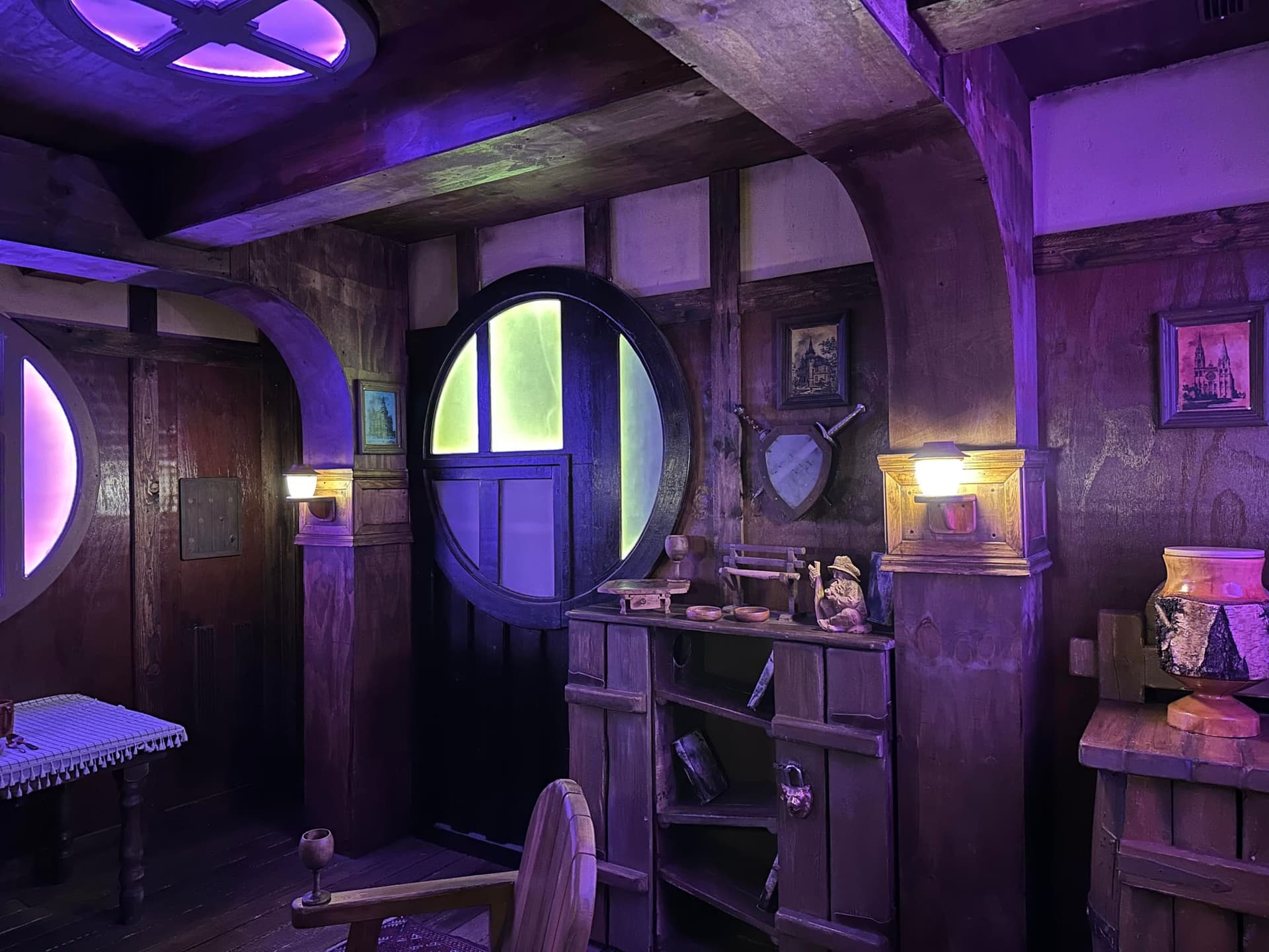 Rundes, grün leuchtendes Fenster und Holzregale in der Halblingshütte im Escape Room Die Abenteuer des Halbling in Rosenheim